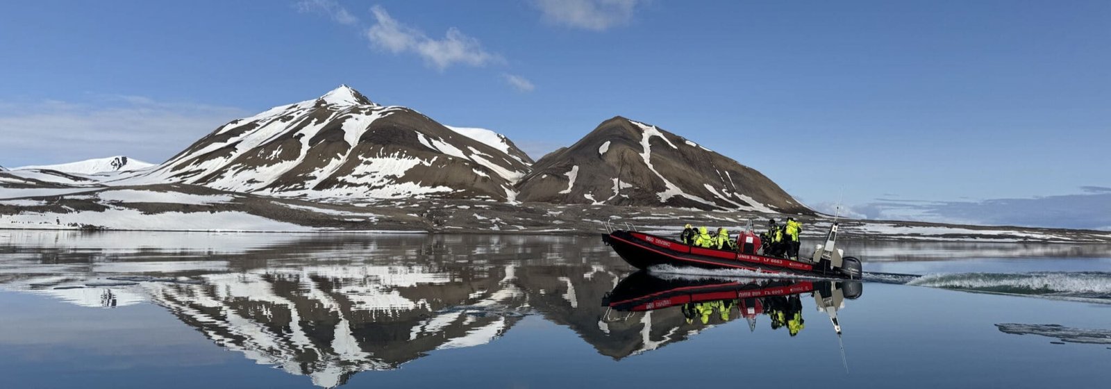 A research boat on a still fjord, mountains mirrored in the water