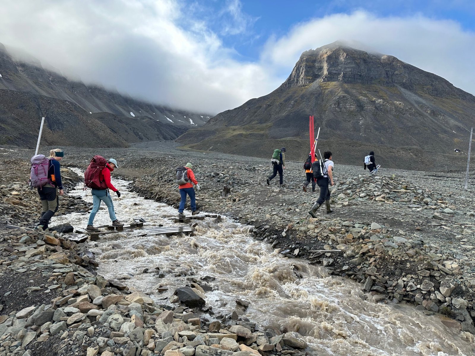 Students hiking along a meltwater river below the mountains